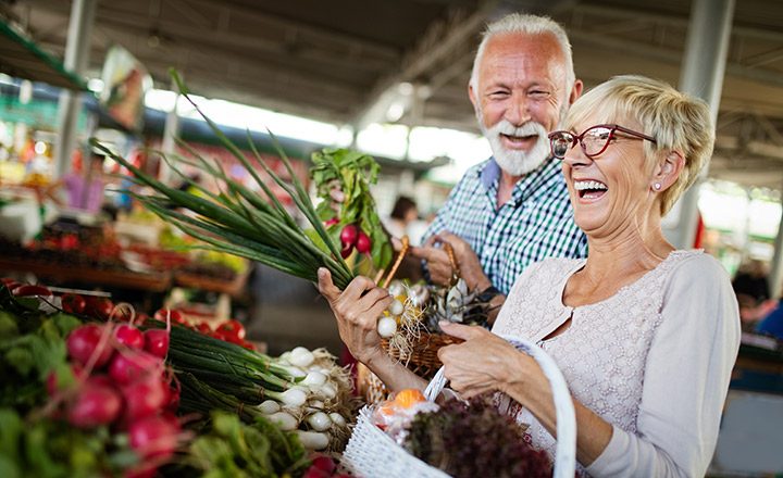 Smiling senior couple holding basket with vegetables at the grocery shop