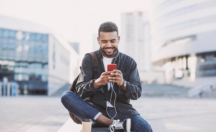 young man sitting with coffee outside with smartphone